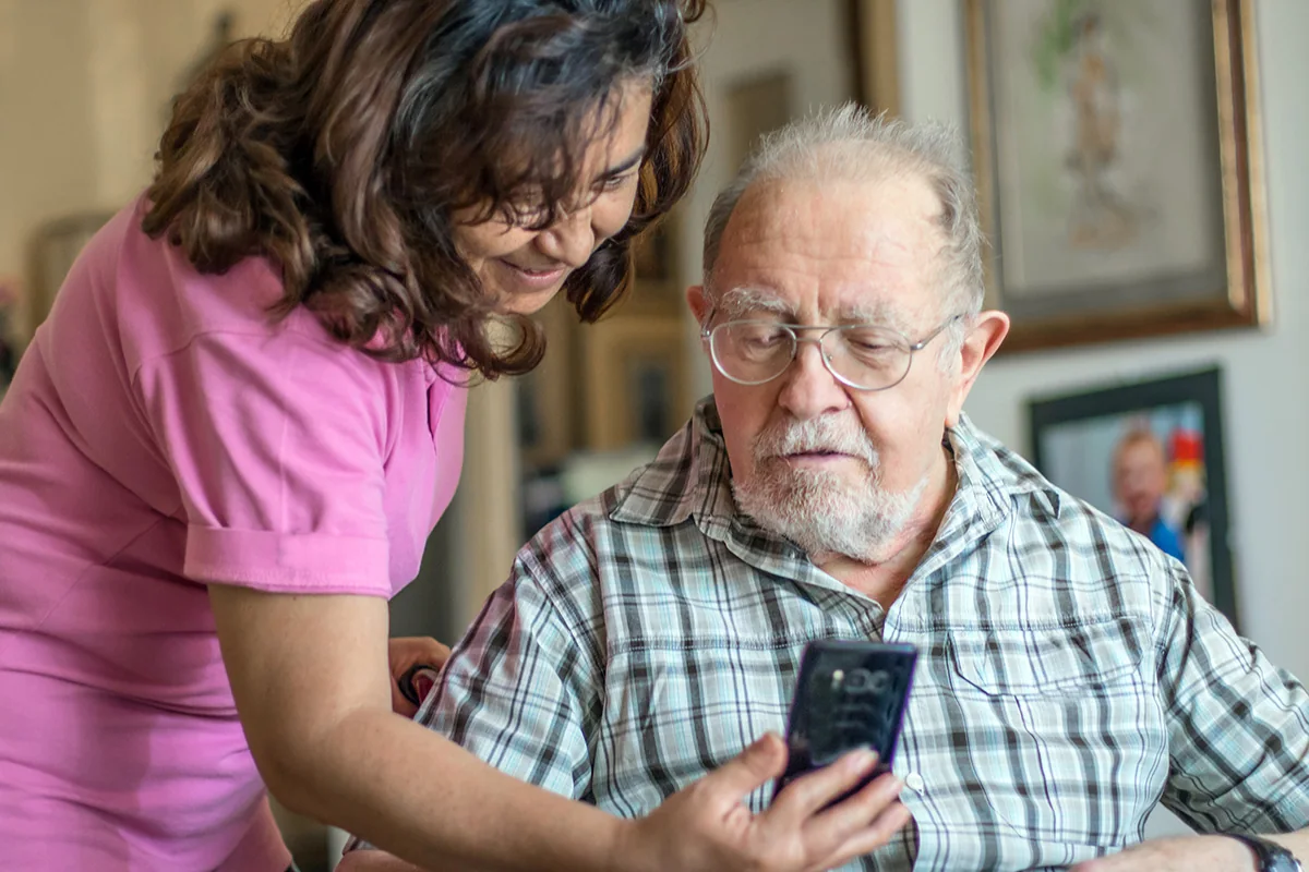 En medarbetare och en äldre person använder en mobiltelefon tillsammans vid en videokonsultation