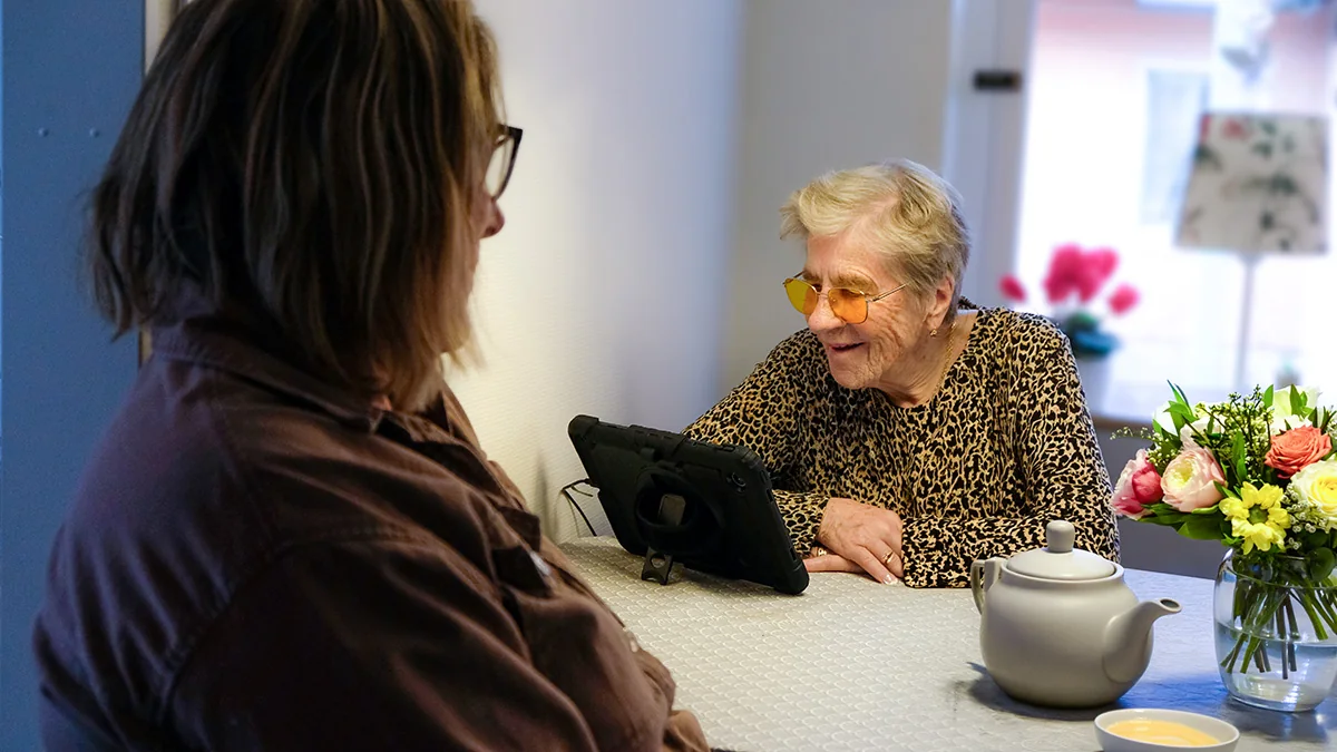 Linnea använder en hembesöksenhet för digital hemtjänst vid köksbordet i Skurup